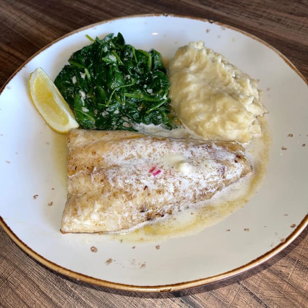 A Lake House Kitchen & Tavern dish with pan-seared fish, mashed potatoes, creamed spinach, and a lemon wedge.