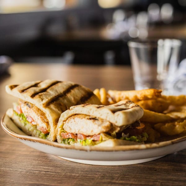 Grilled chicken panini with lettuce, tomato, and fries on a plate at The Lake House Kitchen & Tavern.