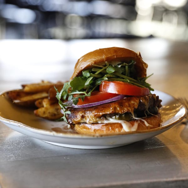 A Lake House Kitchen & Tavern burger with arugula, tomato, onion, and sauce, served with fries.